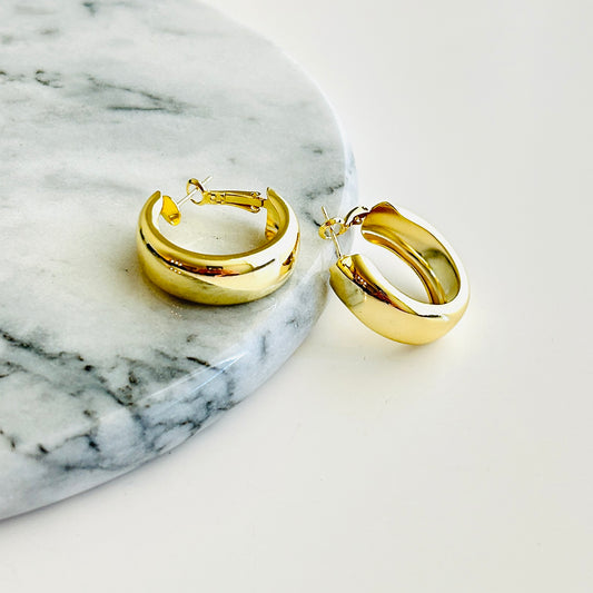 Small gold-plated hoop earrings on a marble background.